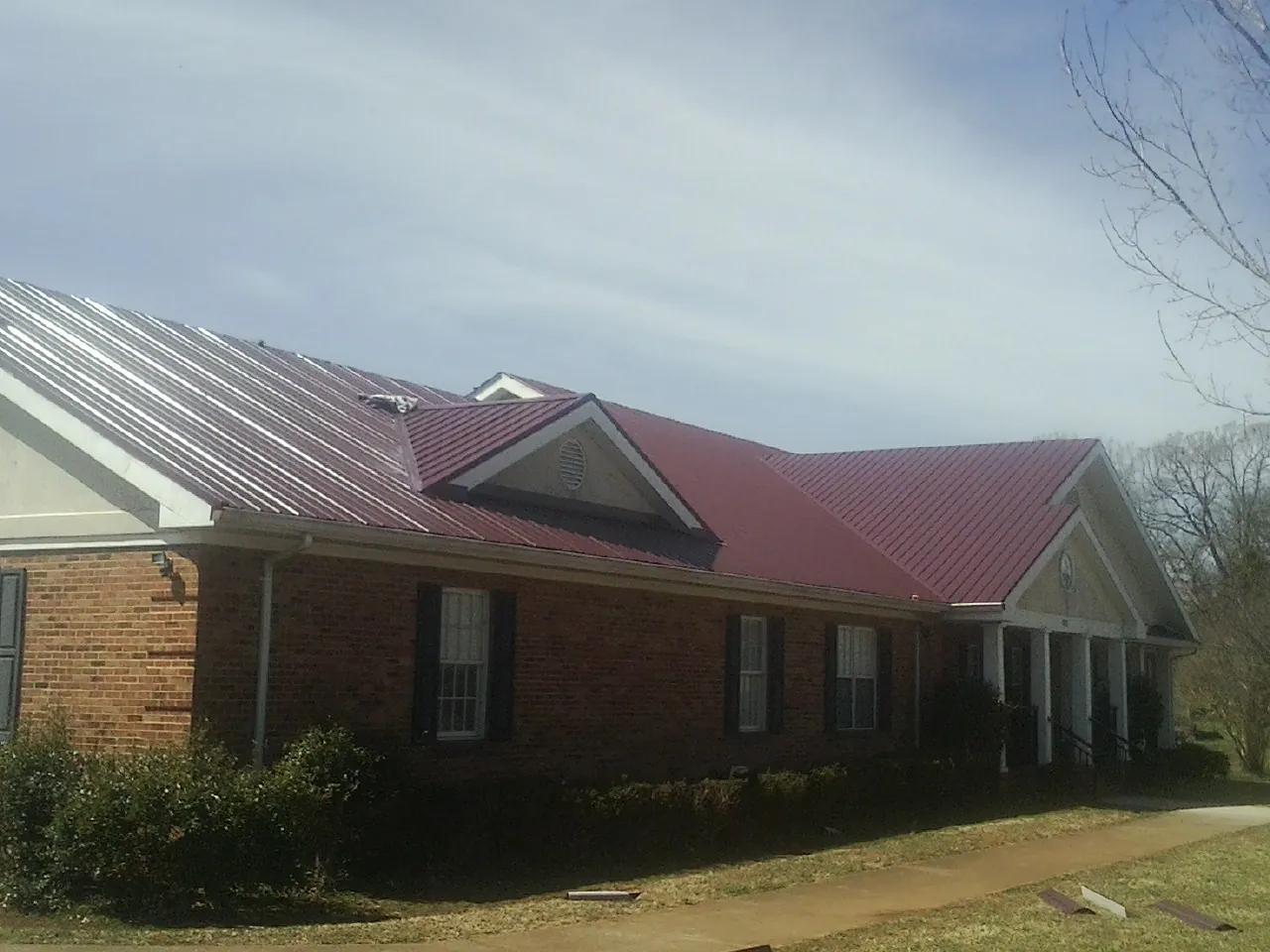 Red metal roof with gabled entries on a long brick building, from a Hail Damage Roof Repair job in Blain