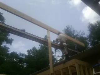 Carpenter setting a ridge beam over a new addition frame in Blain