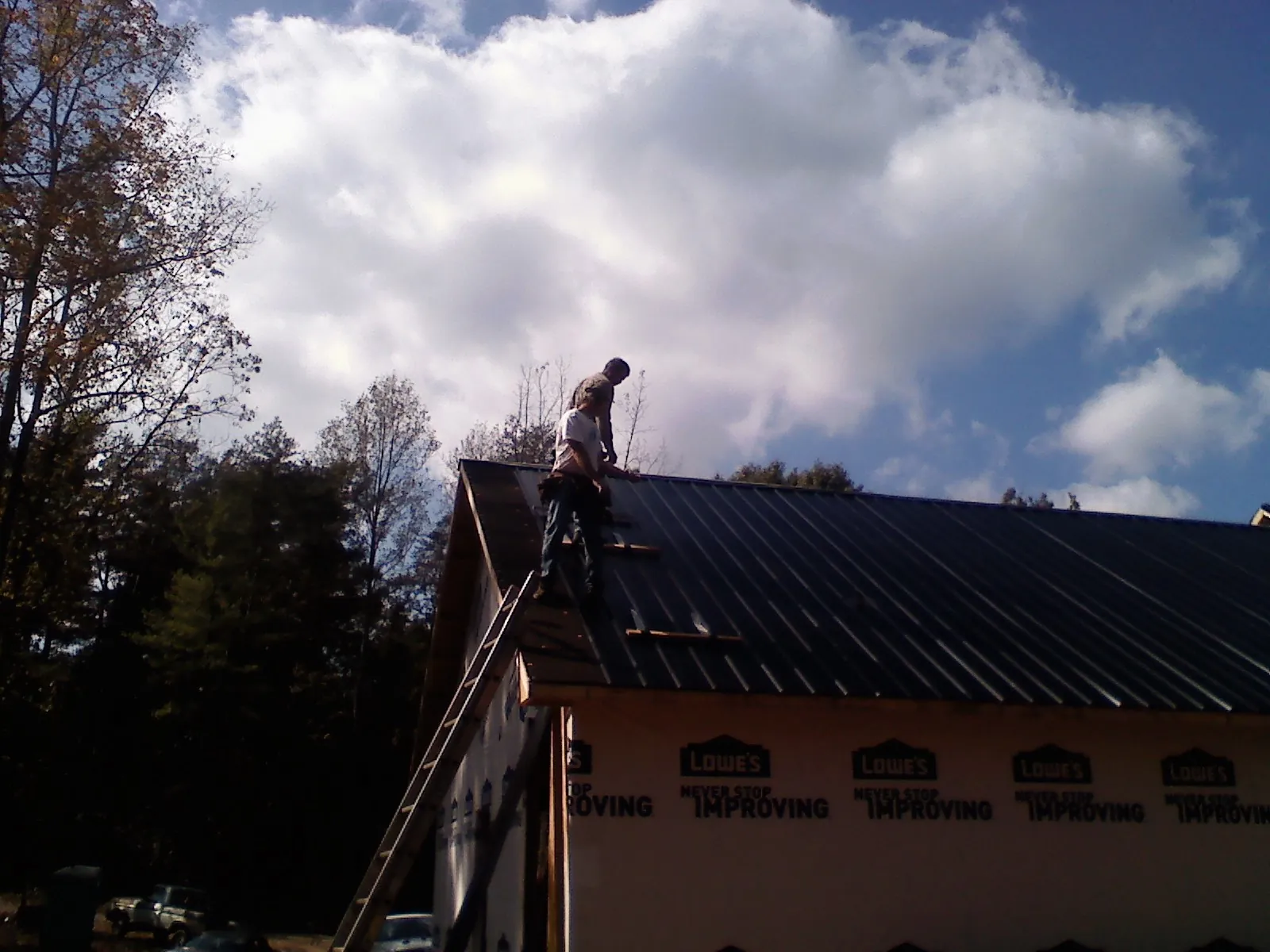 Roofer fastening dark metal panels high against a cloudy sky, from a Roof Inspection job in Blain