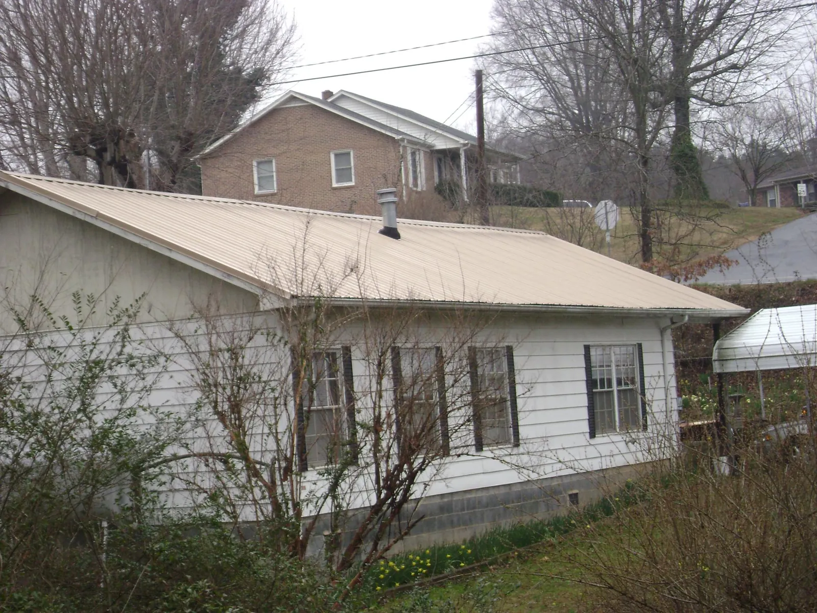 Tan metal roof on a white sided house set into a hillside — Commercial Roofing by Roofing Brothers in Blain