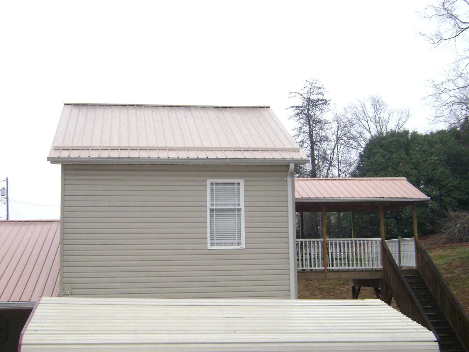 Tan metal roofs on a two story addition and attached porch, from a Roof Replacement job in Blain